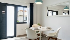 Un comedor con una mesa redonda, dos sillas blancas, una planta en maceta y un espejo grande en la pared.