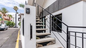 Un edificio moderno con fachada blanca, una escalera de metal negra y un vehículo estacionado en la calle.