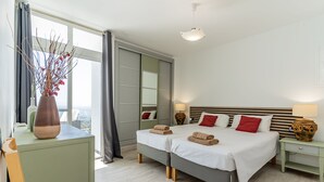 Habitación de hotel moderna con dos camas, un ventanal con vistas, un escritorio y un florero con flores.