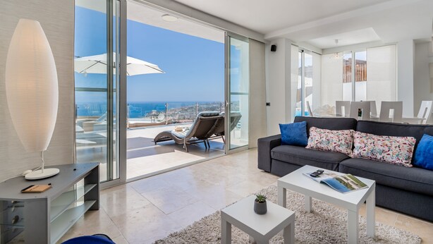 Un moderno salón con un sofá gris, una mesa de centro blanca y un ventanal con vistas a la ciudad.