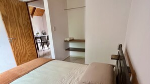 Ein Schlafzimmer mit Holzbalkendecke, einem Bett mit beige farbenen Textilien, einem Holz-Kopfteil und einem kleinen Tisch mit Stühlen im Hintergrund.