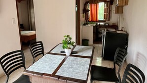 Ein Essbereich mit einem Holztisch und Stühlen, einer Topfpflanze und einer Küche im Hintergrund.