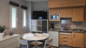 A compact kitchen with a microwave, a coffee maker, and a small refrigerator. There is a dining table with chairs and a potted plant on the counter. - Estudio Premium Sierra Nevada (Sierra Nevada)