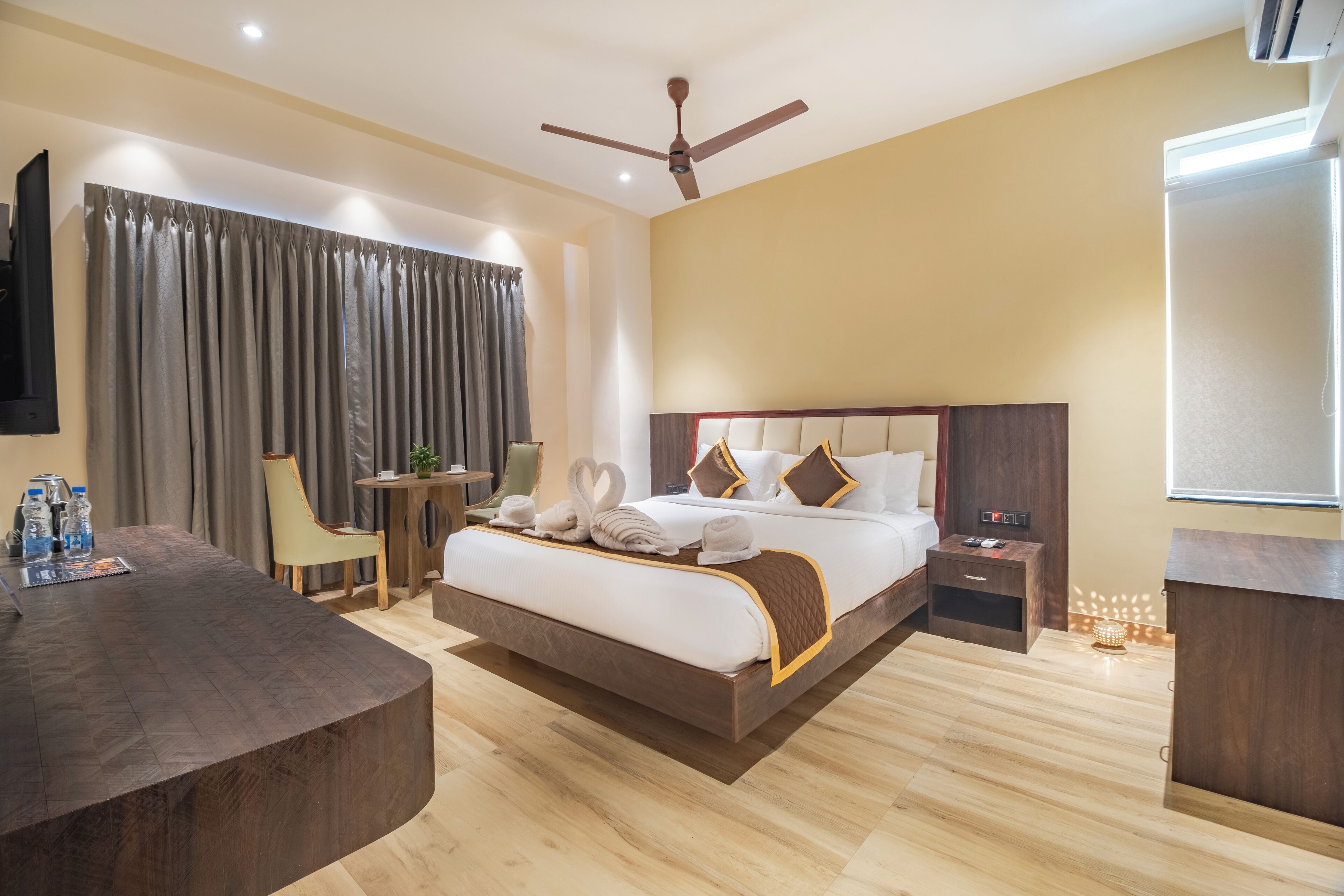 Une chambre d’hôtel avec un grand lit, un bureau, une chaise, une petite table et un ventilateur de plafond.
