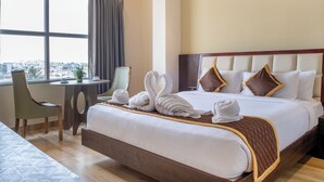 Quarto de hotel com uma cama grande, uma escrivaninha com cadeira e vista para a cidade através de uma janela ampla.
