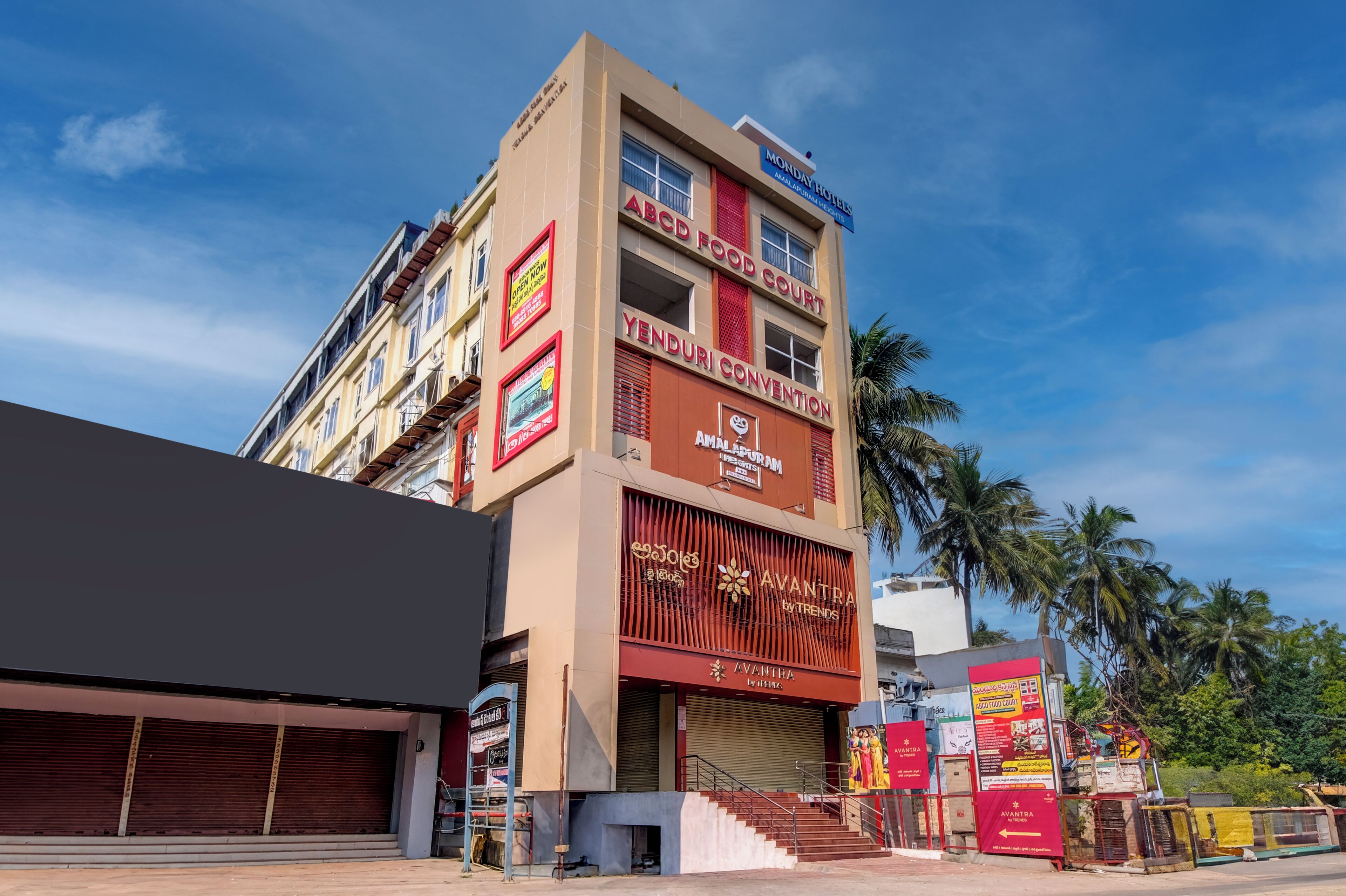 Un edificio de varios pisos con letreros que indican 'Monday Hotel', 'ABC Food Court', 'Yenduri Convention' y 'Avantha by Aishwarya'.