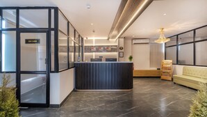 Um hall de hotel moderno com uma mesa de recepção, área de estar e escadaria para os andares superiores.