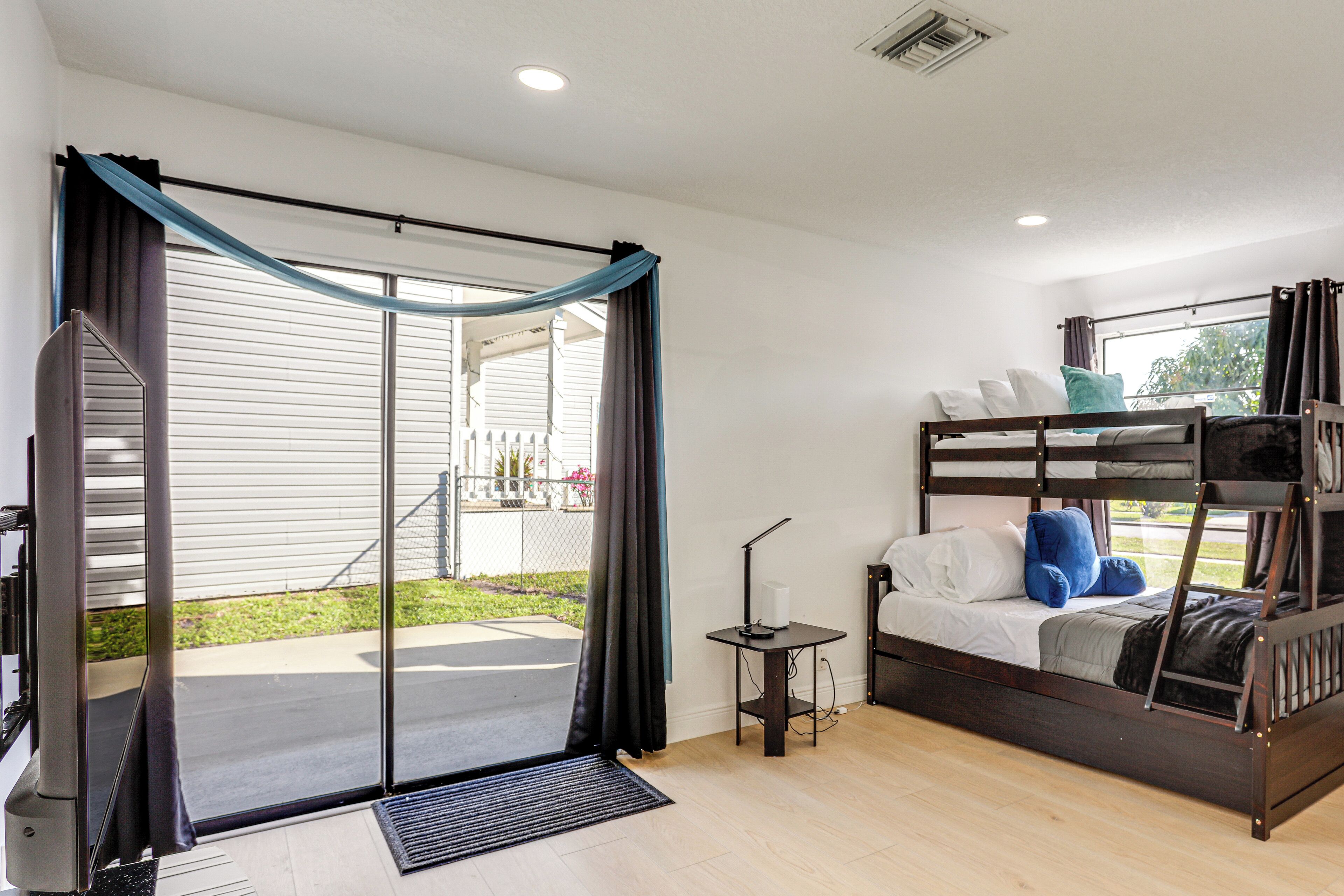 Quarto com beliche, escrivaninha com luminária e porta de vidro corria para um pátio.