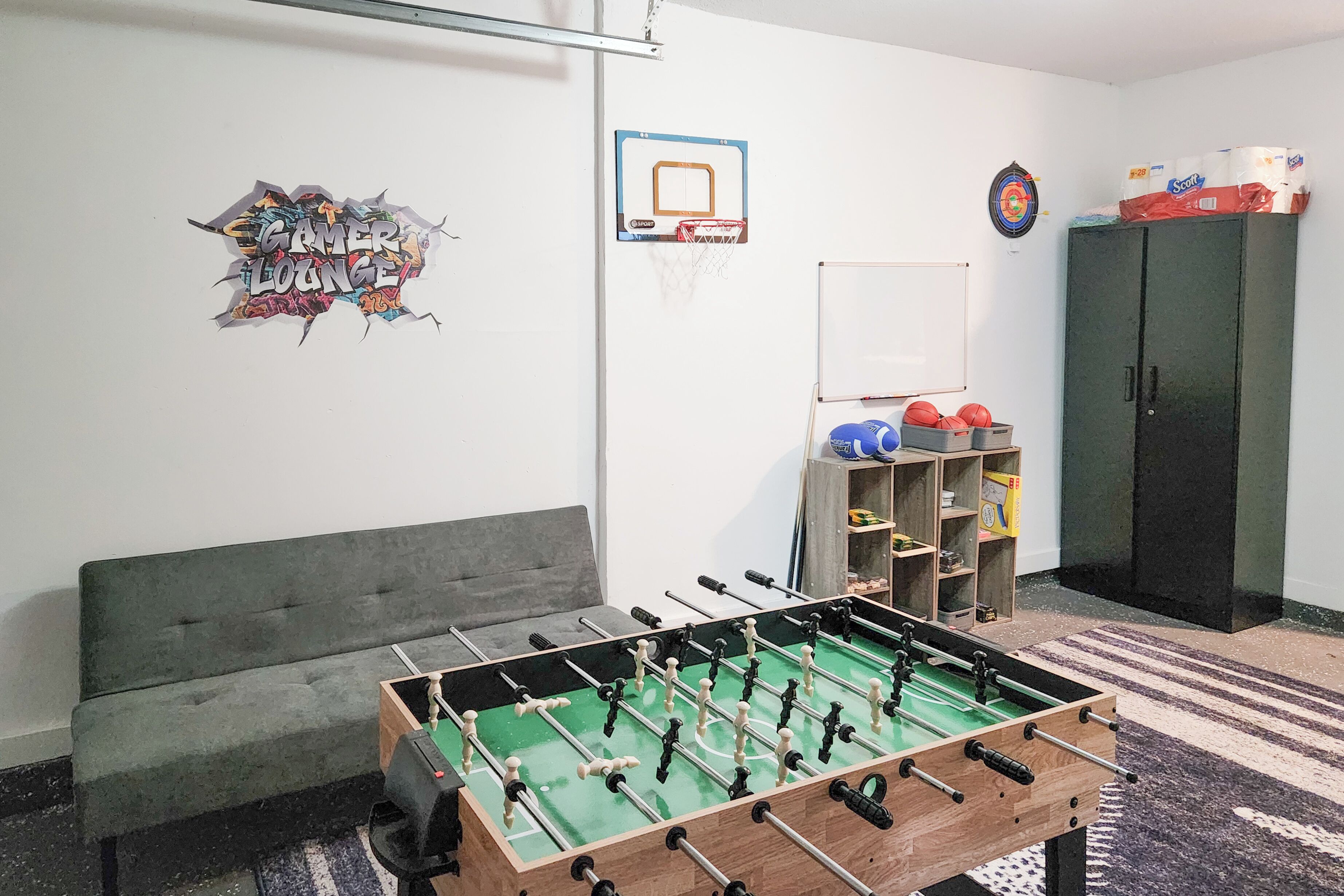 Une pièce équipée d’un baby-foot, d’un canapé, d ’un jeu de fléchettes et d’un meuble.