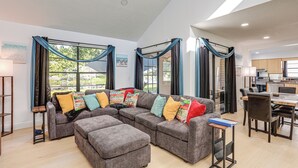 Een ruime woonkamer met een hoekbank, een eethoek en een keuken op de achtergrond.