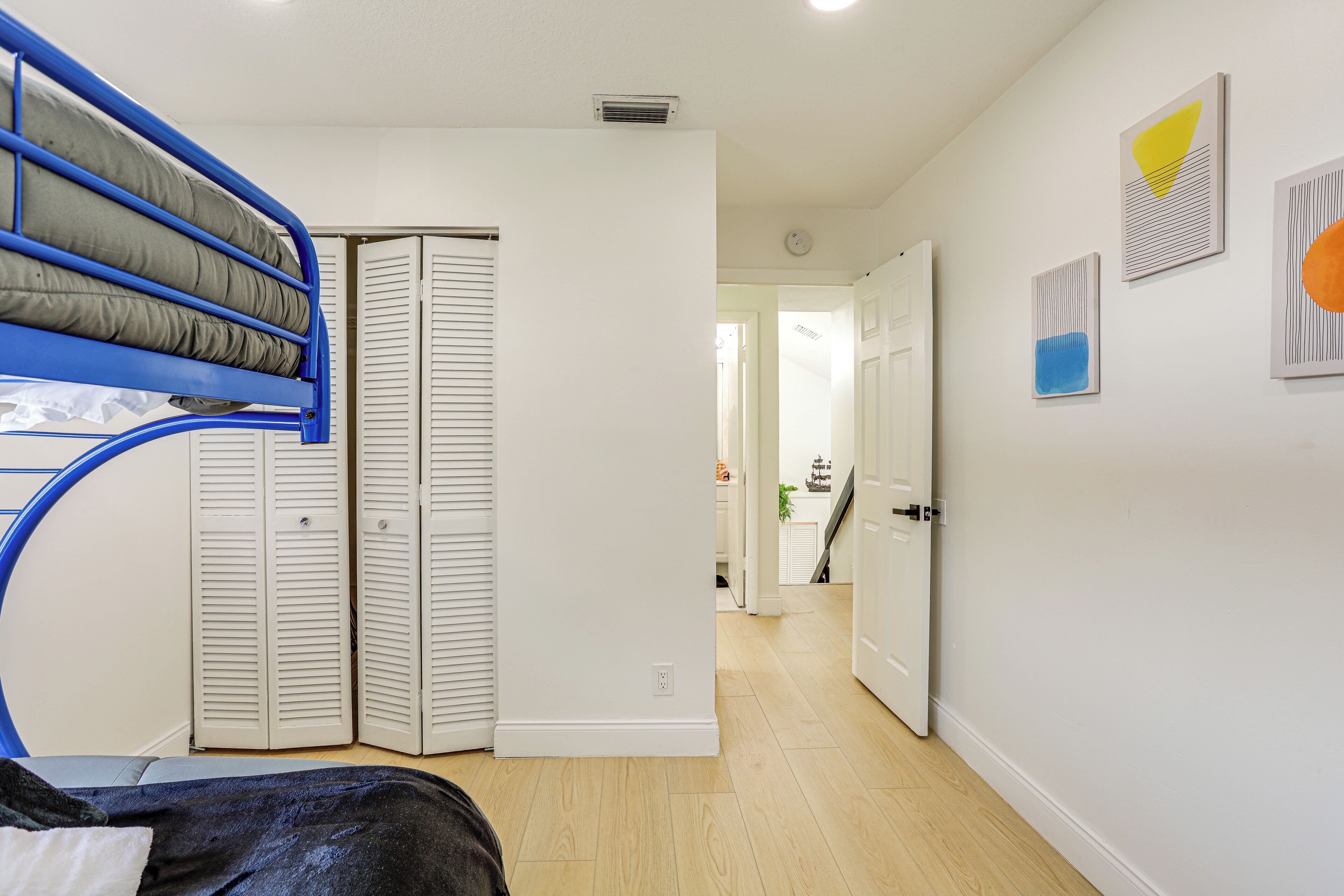 A room with a bunk bed, white walls, and a hallway leading to another room.