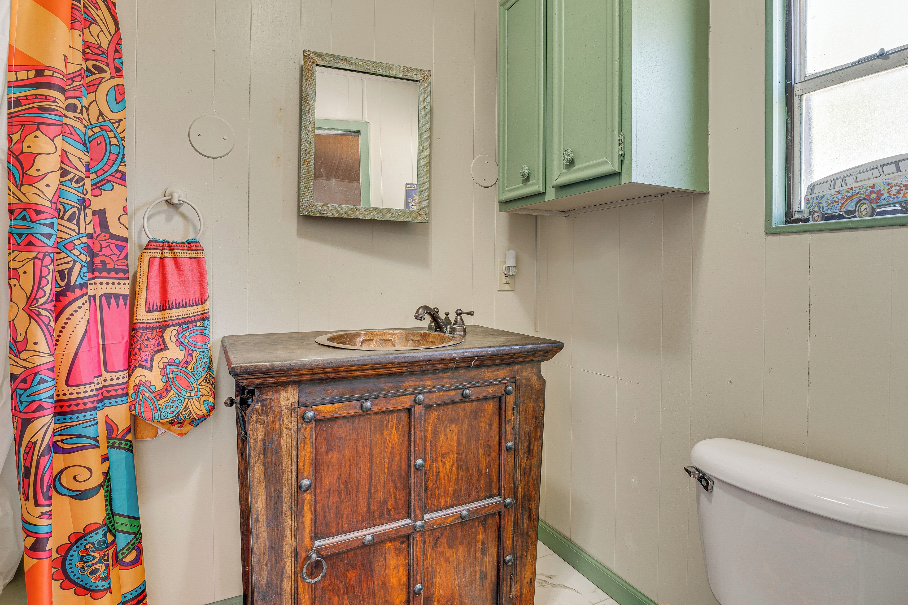 Un baño con tocador de madera, lavamanos, espejo y retrete.