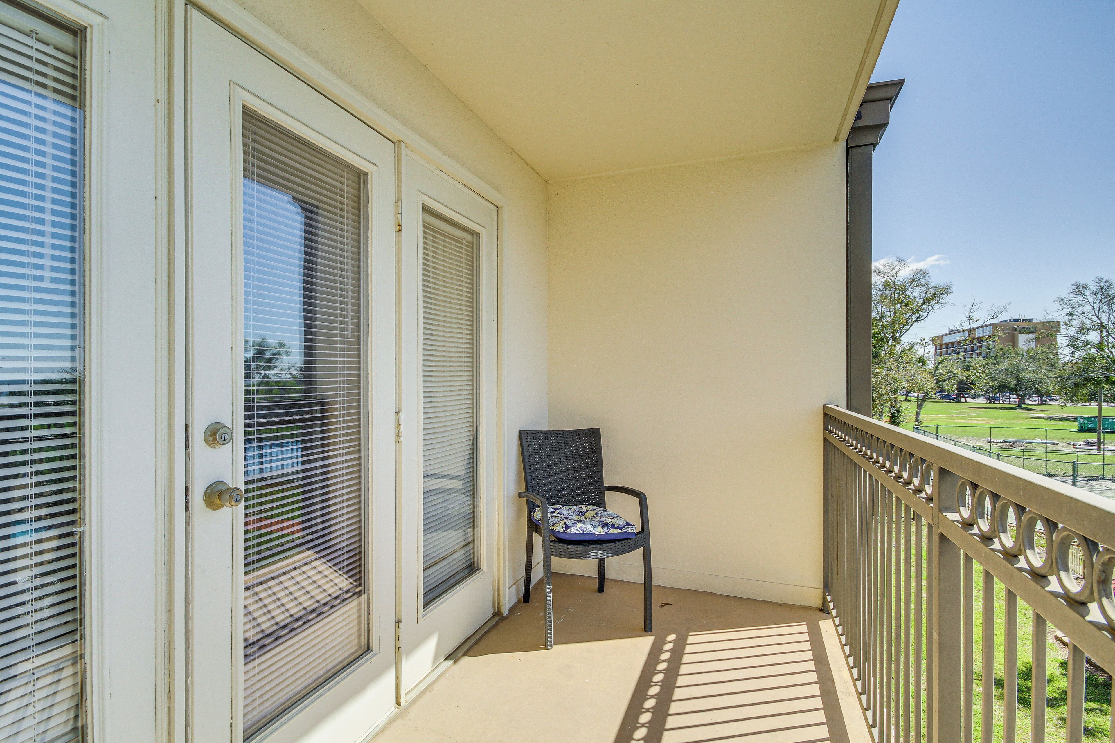 Een balkon met een stoel, een deur met een raam en uitzicht op een park en gebouwen.