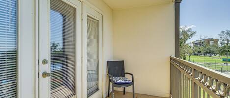 Een balkon met een stoel, een deur met een raam en uitzicht op een park en gebouwen.