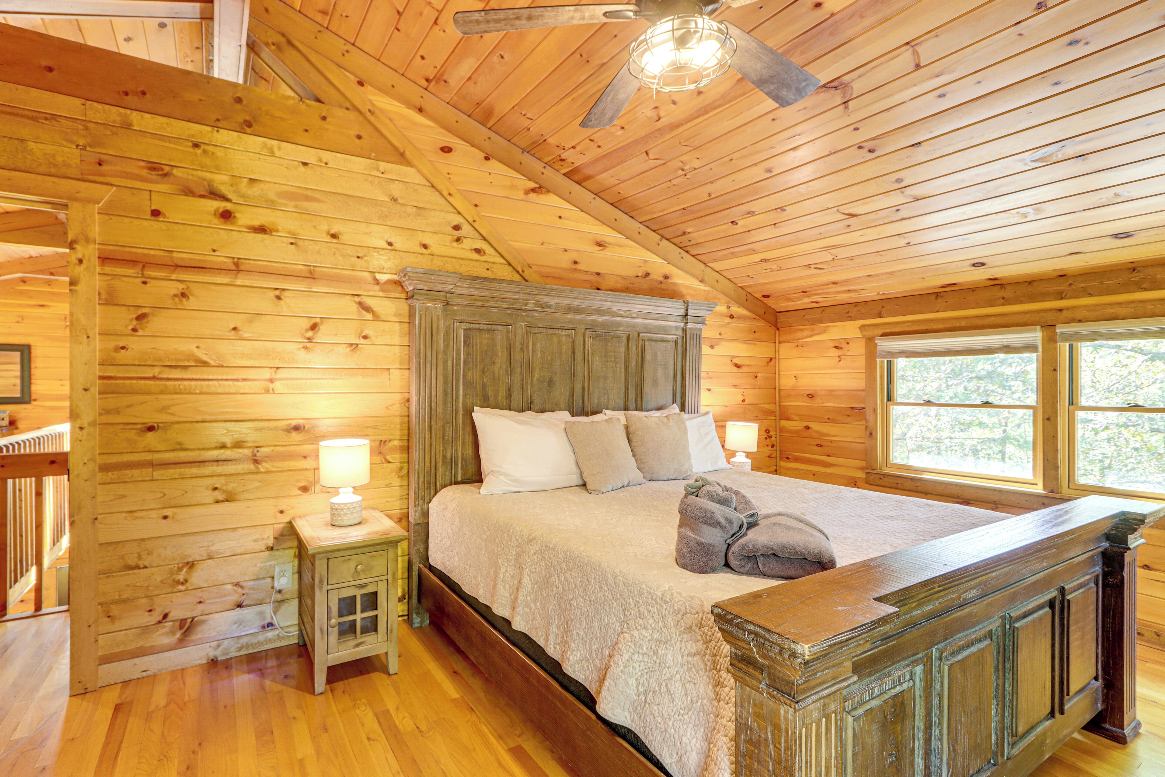 A wooden cabin bedroom with a bed, nightstand, and a ceiling fan.