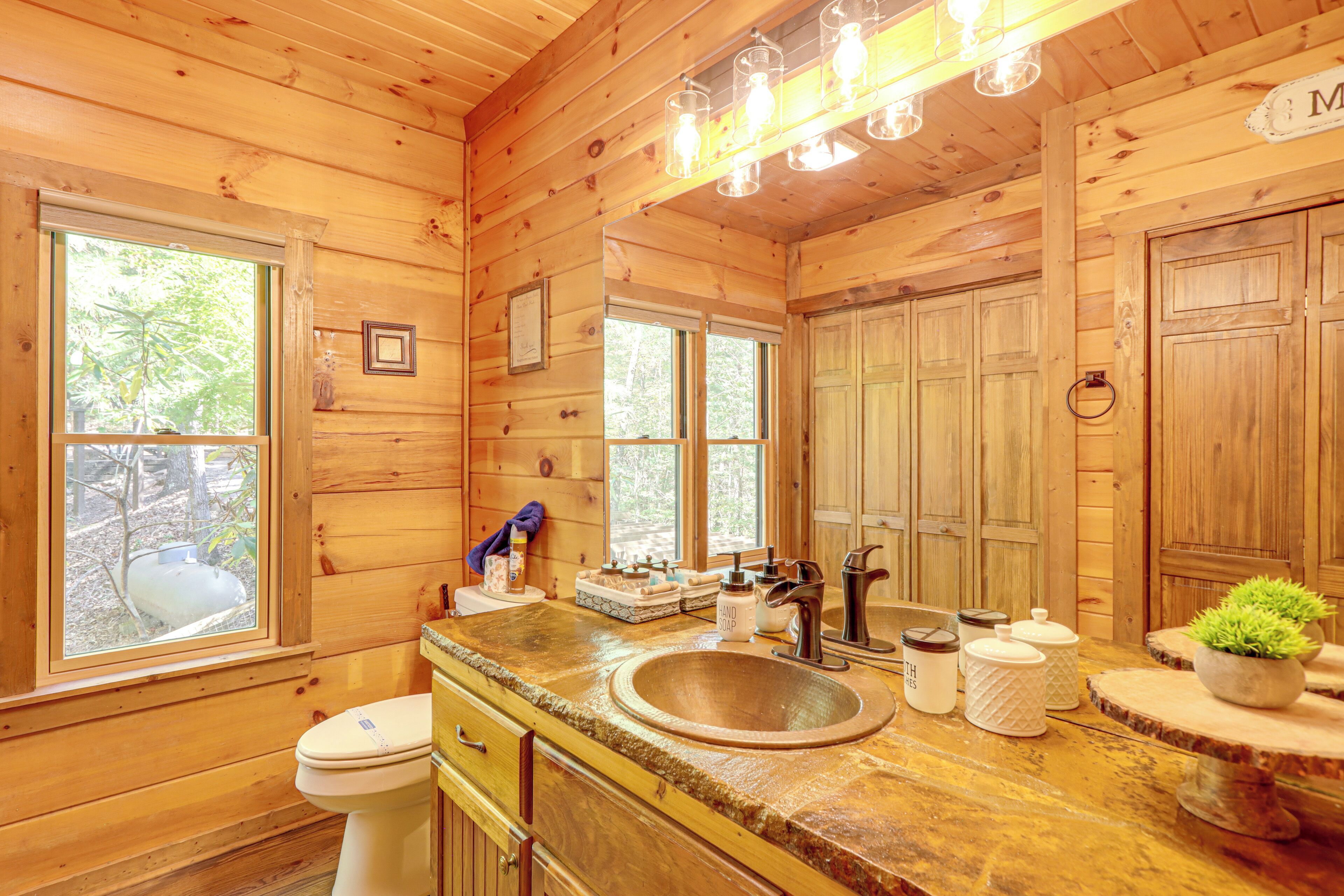 A wooden cabin bathroom with a sink, toilet, and windows.