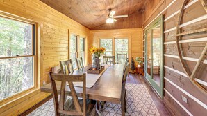 A wooden cabin interior with a dining table, chairs, a ceiling fan, and large windows. - Blue Ridge Cabin w/ Hot Tub, Fire Pit, & Game Room (Cherry Log)