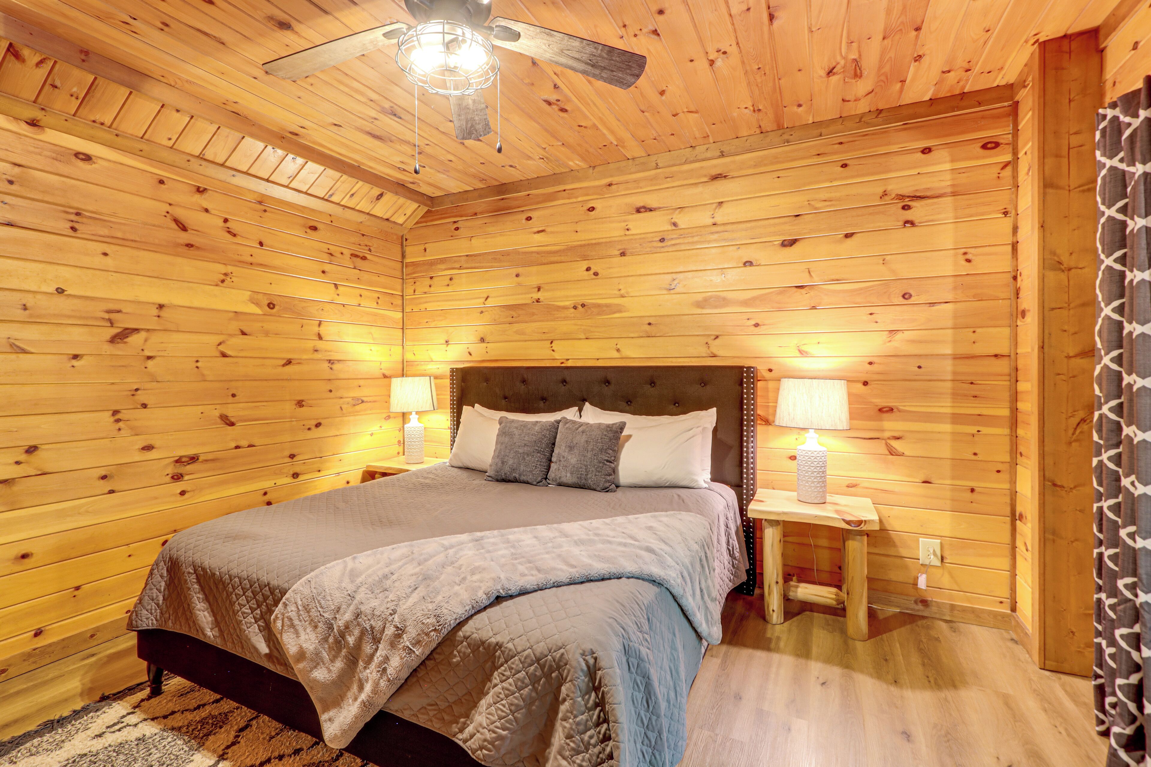 A wooden-paneled bedroom with a bed, two bedside lamps, and a ceiling fan.