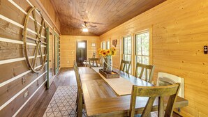 A wooden interior with a dining table, chairs, and a large wooden wheel. - Blue Ridge Cabin w/ Hot Tub, Fire Pit, & Game Room (Cherry Log)