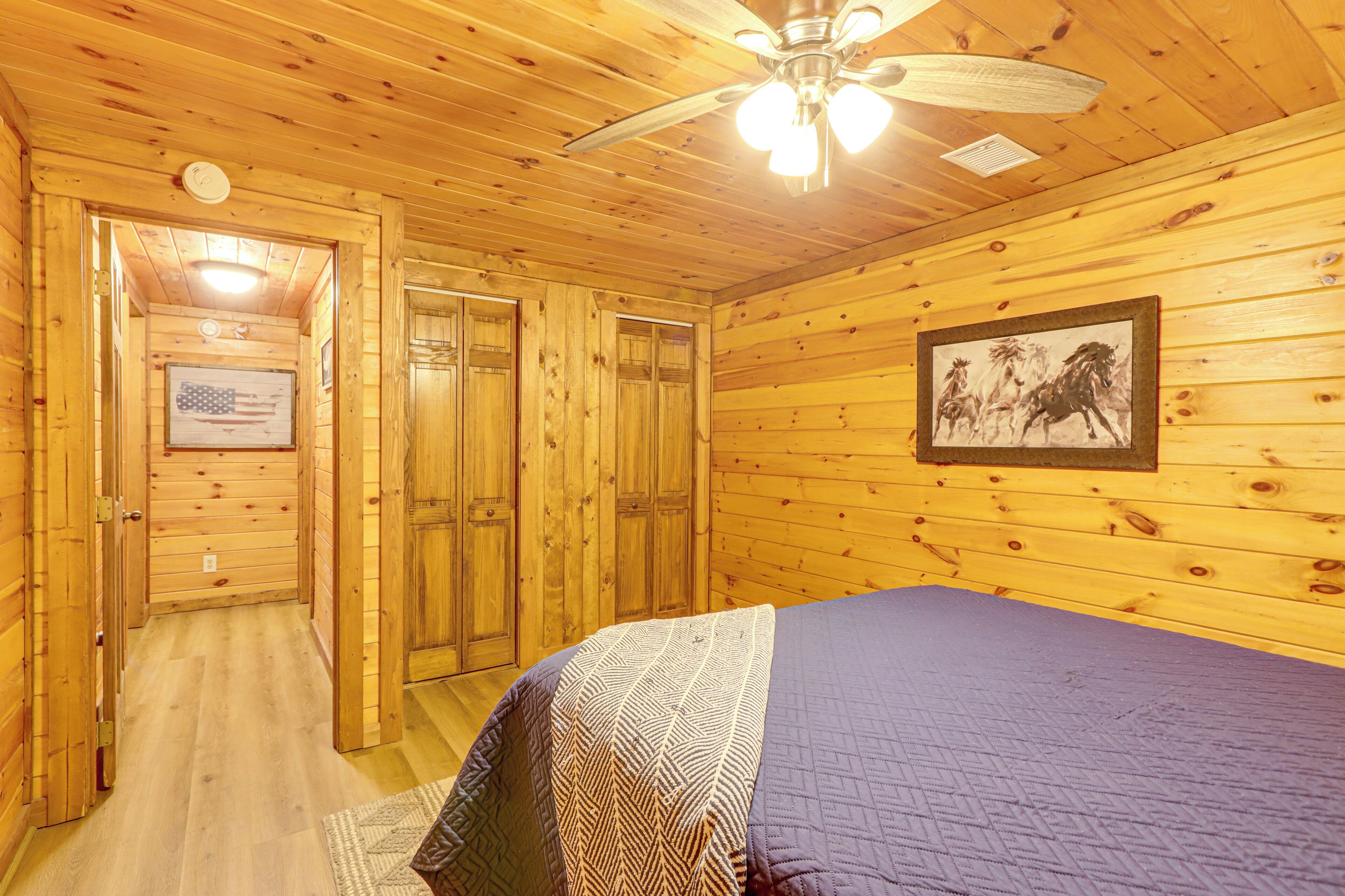 A wooden cabin room with a bed, a ceiling fan, and a framed picture on the wall.