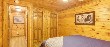 A wooden cabin room with a bed, a ceiling fan, and a framed picture on the wall.