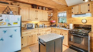 A wooden cabin kitchen with a refrigerator, microwave, stove, and wooden cabinets. - Lamoine Cabin w/ Deck ~ 16 Mi to Acadia Natl Park (Ellsworth)