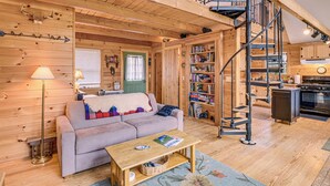 A cozy log cabin interior with a living room, a staircase, a kitchen, and a bookshelf. - Lamoine Cabin w/ Deck ~ 16 Mi to Acadia Natl Park (Ellsworth)