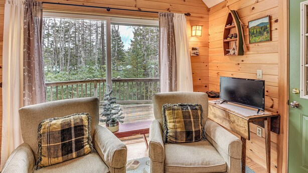 A cozy cabin interior with two armchairs, a television, a small Christmas tree, and a wooden shelf with decorative items. - Lamoine Cabin w/ Deck ~ 16 Mi to Acadia Natl Park (Ellsworth)