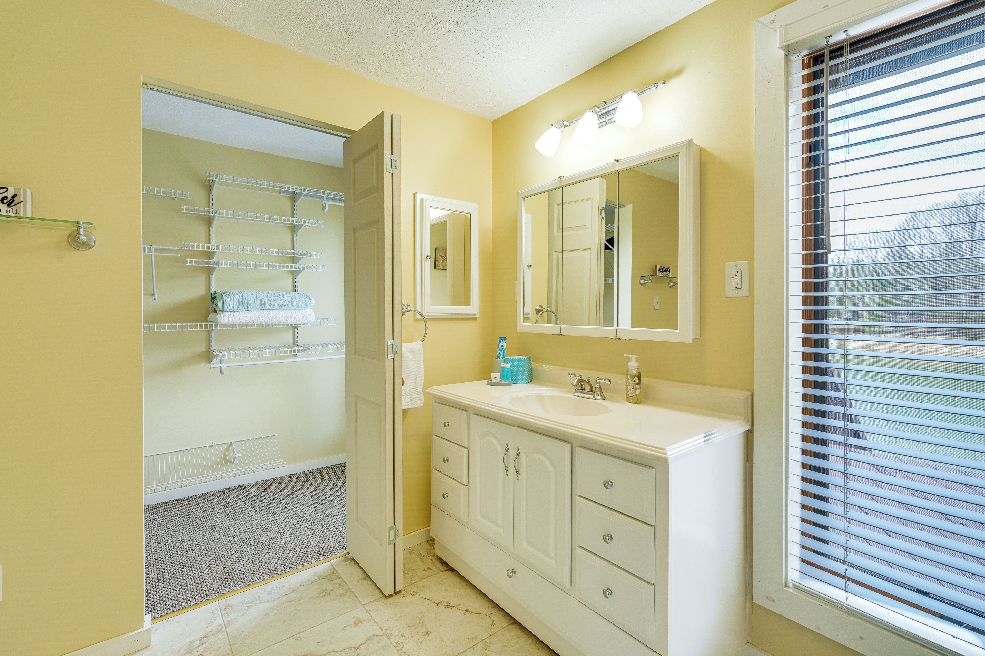 A bathroom with a white vanity, a large mirror, and a window with blinds.