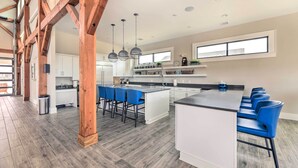 A spacious kitchen with a central island, blue bar stools, and wooden beams. - Coastal Beaufort Abode - Pool Access, Near Beaches (Beaufort)