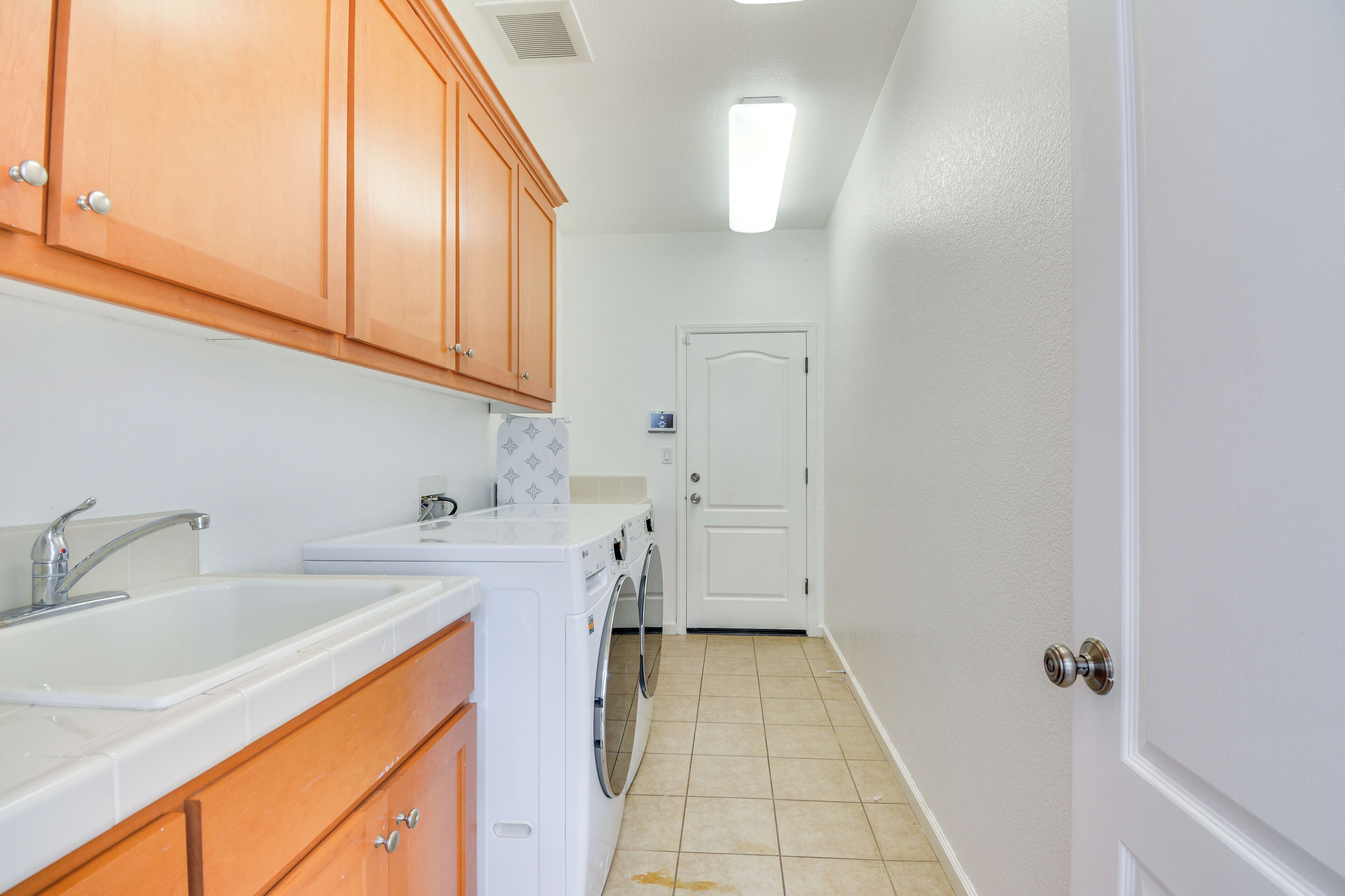 A kitchen with wooden cabinets, a sink, a washing machine, and a door in the background.