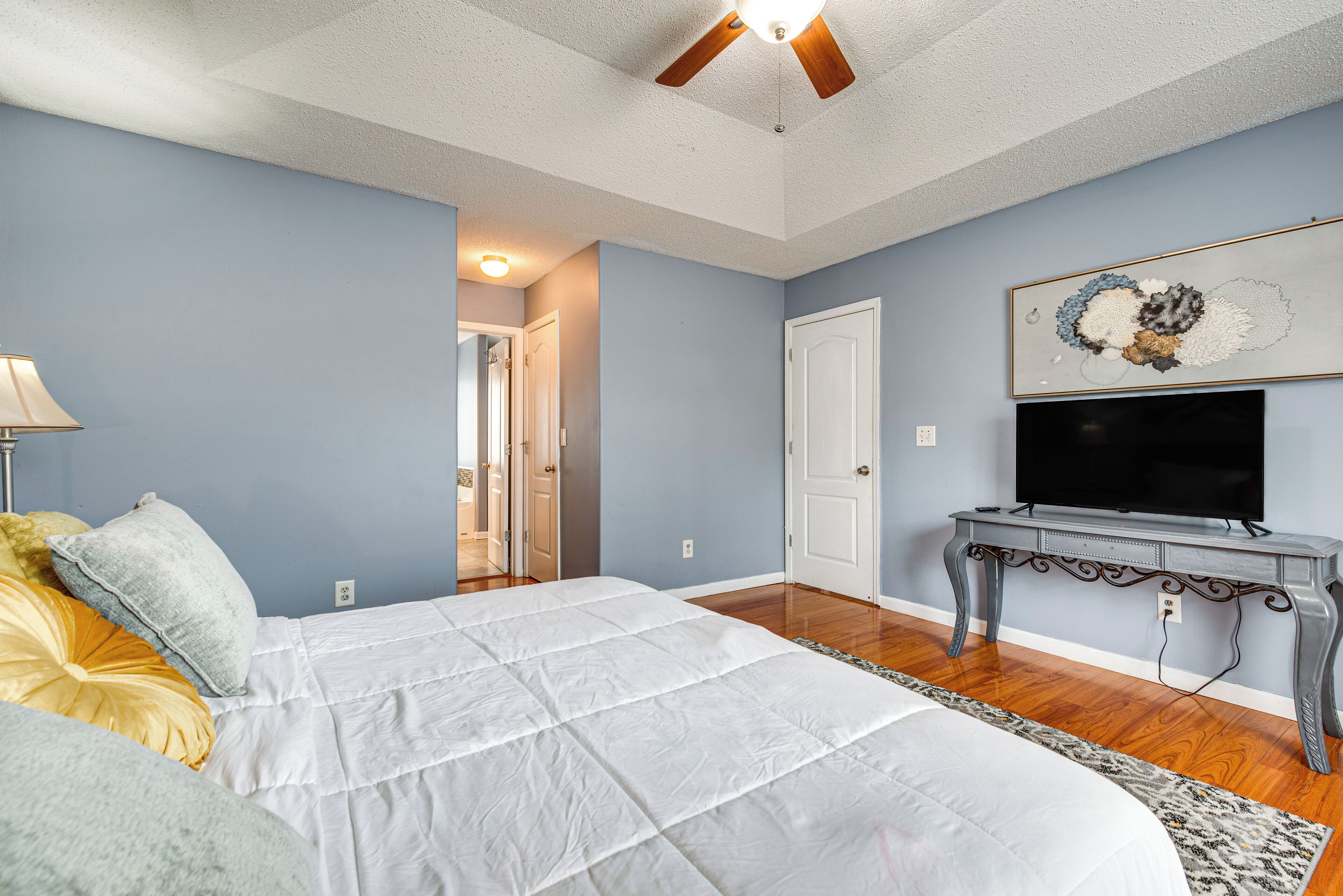 A bedroom with a bed, a TV on a stand, and a door leading to another room.