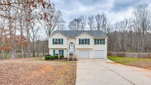 A two-story house with a garage, a front yard with a ladder, and a wooden fence.
