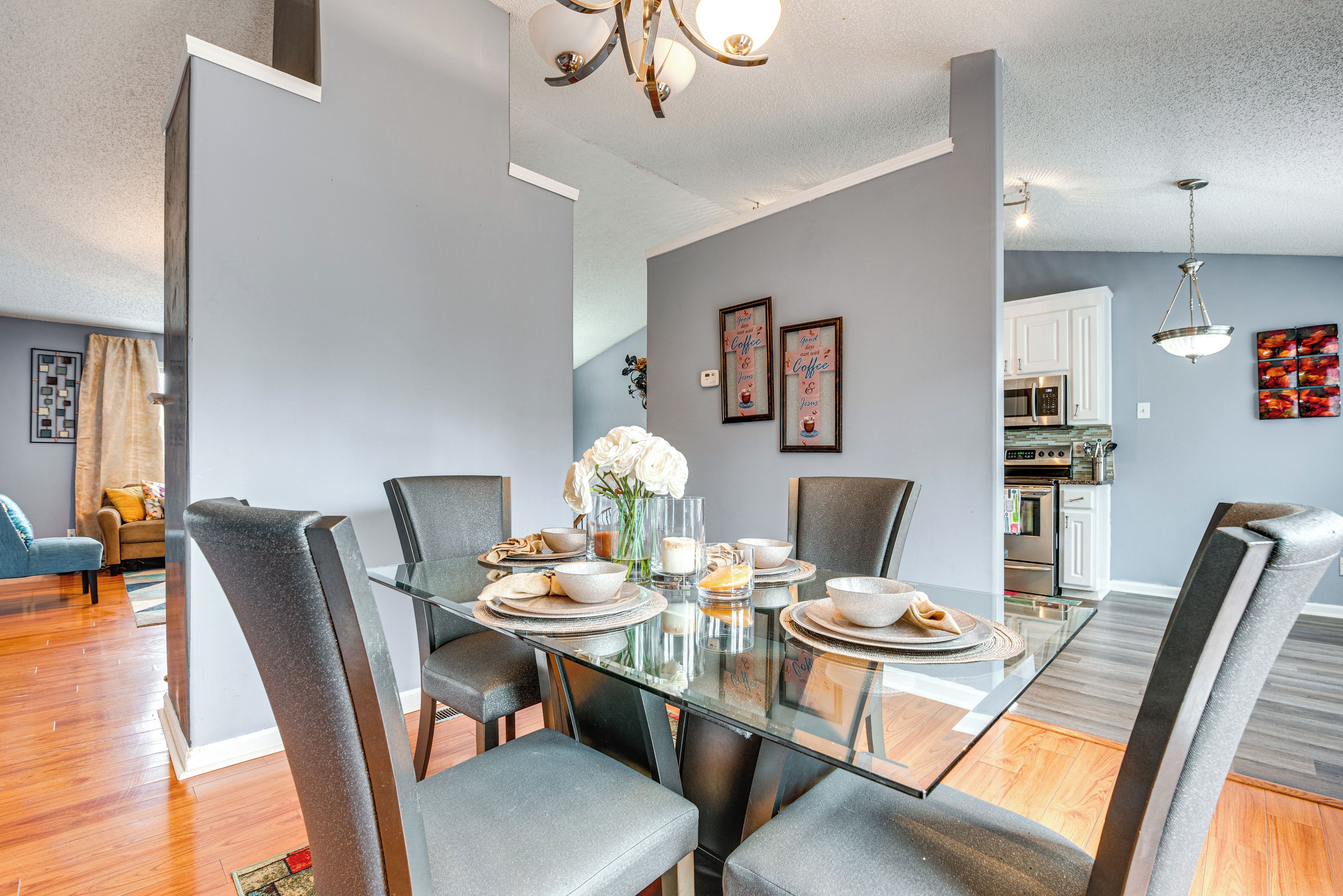 A modern dining area with a glass table, grey upholstered chairs, and a vase of white flowers.