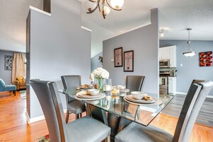 A modern dining area with a glass table, grey upholstered chairs, and a vase of white flowers.
