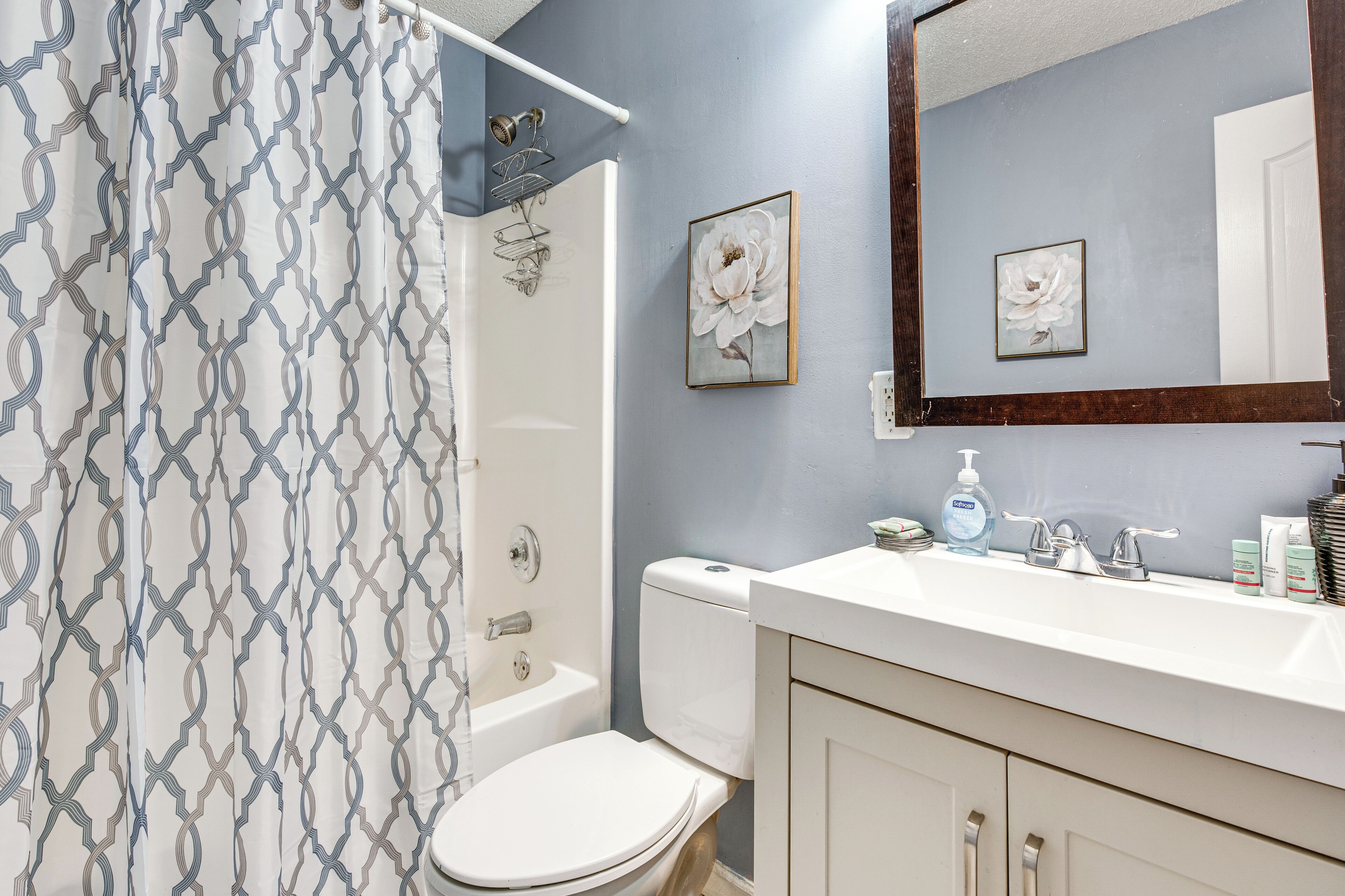 A bathroom with a shower curtain, toilet, sink, and mirror.