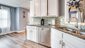 A modern kitchen with white cabinets, granite countertops, stainless steel appliances, and a backsplash with mosaic tiles.