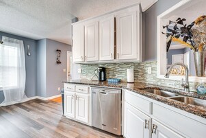 A modern kitchen with white cabinets, granite countertops, stainless steel appliances, and a backsplash with mosaic tiles.