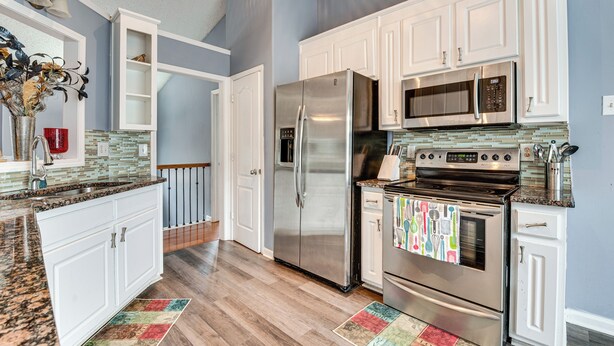 A modern kitchen with white cabinets, stainless steel appliances, and a tiled backsplash.