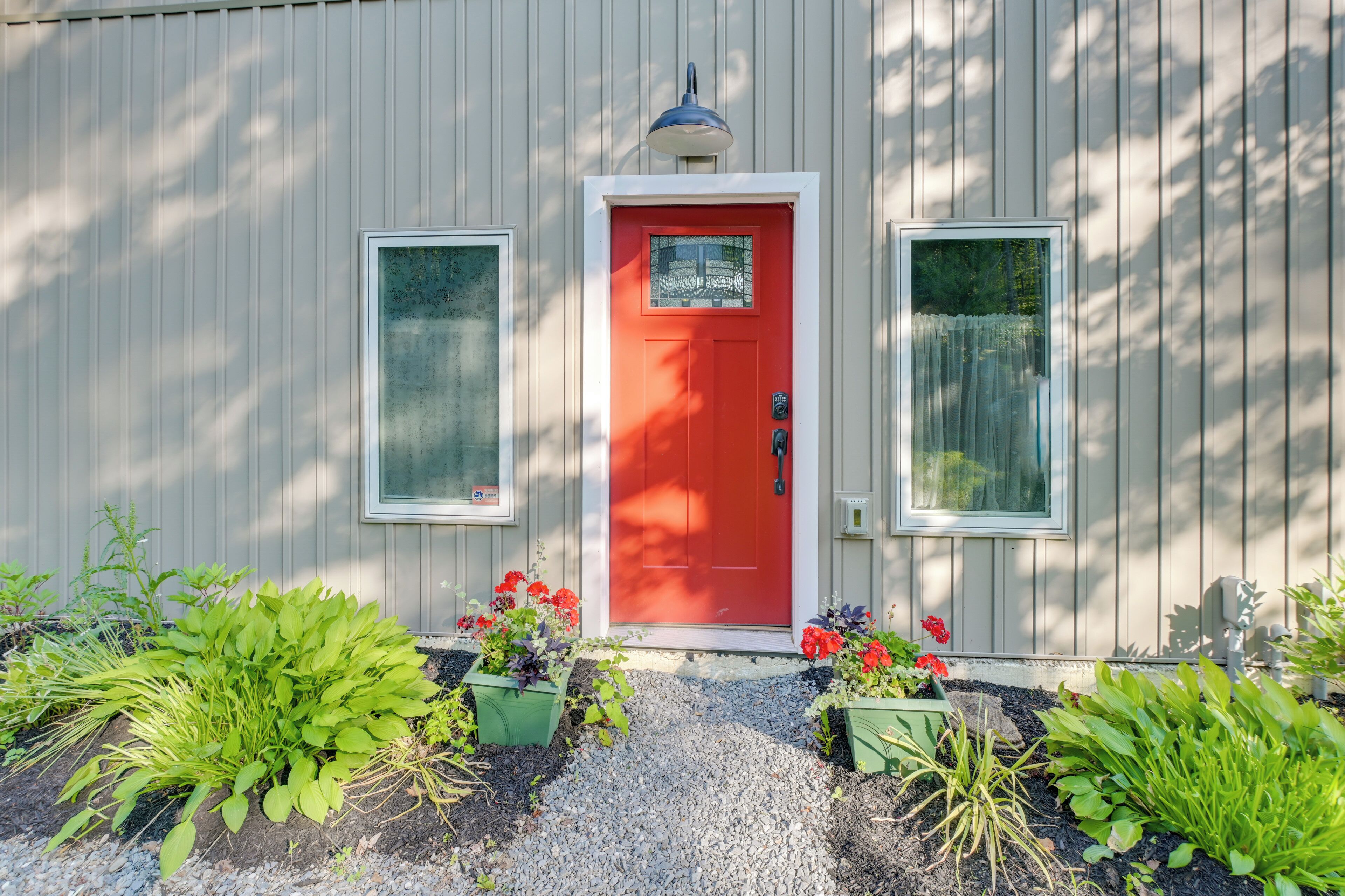 A building with a red door, two windows, and a gravel pathway with plants.