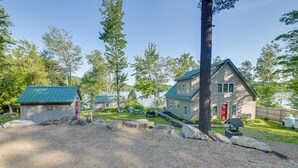 A cabin with a green roof, a red door, and a small shed in a wooded area. - Lakefront Bucksport Home w/ Fire Pit + Gas Grill! (Bucksport)