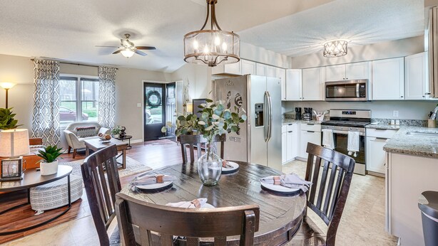 A modern kitchen with white cabinets, a central island, and a dining area with a round table and chairs. - Mebane Home w/ Private Yard: Steps to Downtown! (Mebane)
