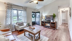 A spacious living room with a ceiling fan, a sofa, a coffee table, and a television on a wooden stand. - Mebane Home w/ Private Yard: Steps to Downtown! (Mebane)
