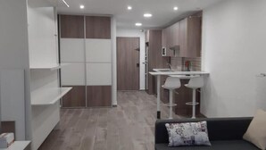 A modern, compact living space with a kitchenette, a dining area, and a sofa with a decorative pillow. - Studio PREMIUM Vera Playa Naturist  (Vera)