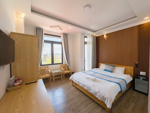 A hotel room with a wooden bed, a desk, a television, and a window with curtains.