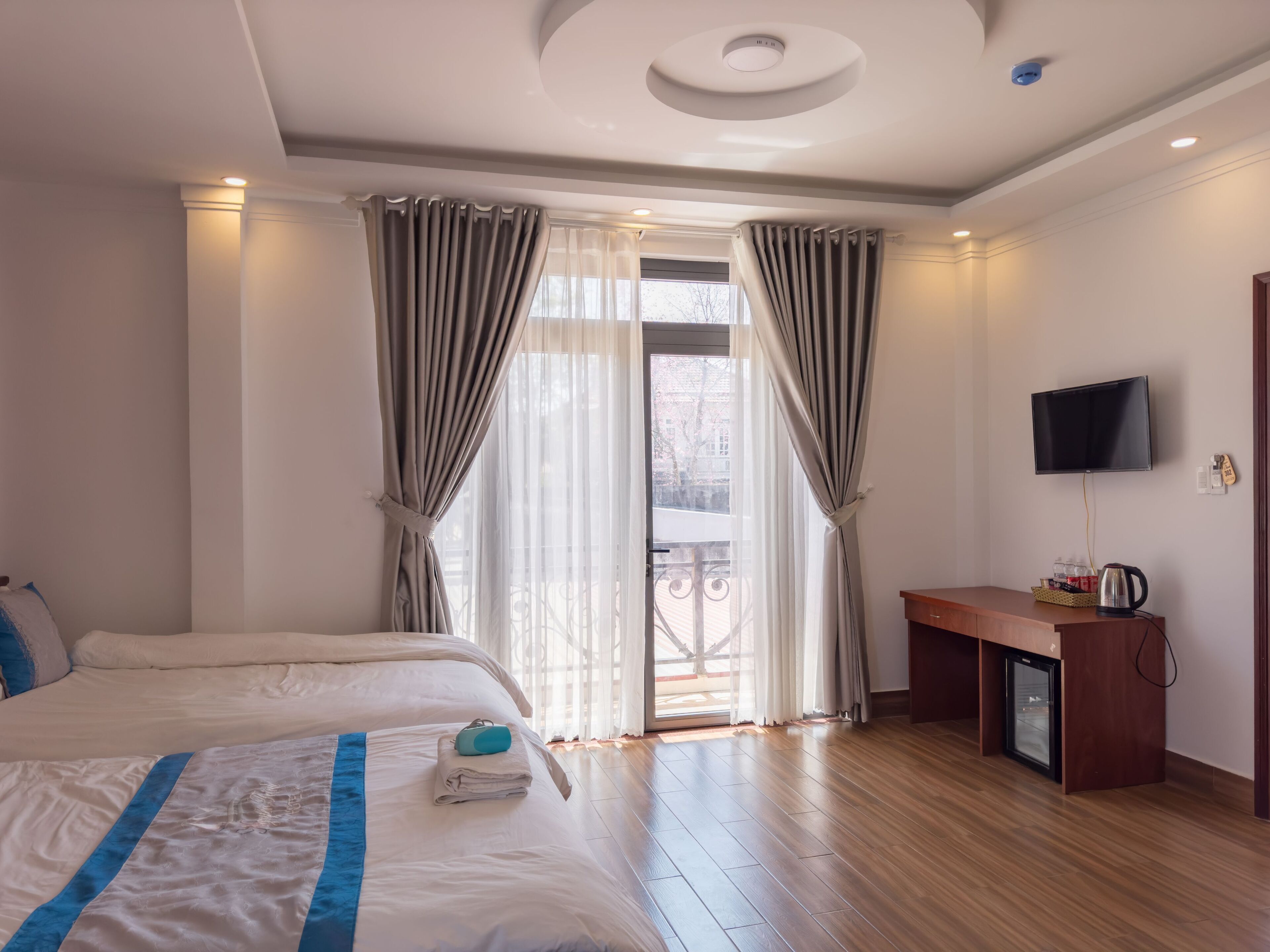 A hotel room with a large bed, a desk with a kettle, a TV, and a balcony view.