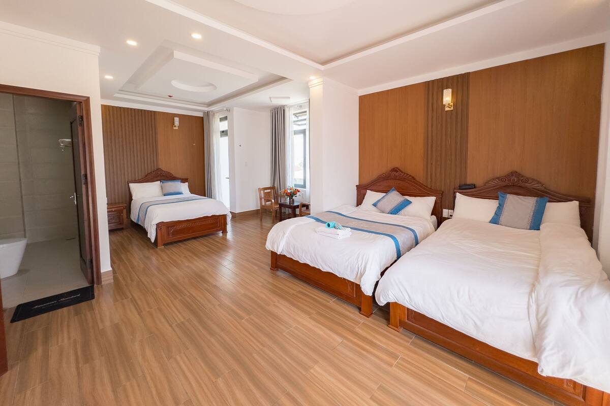 A hotel room with two wooden beds, a wooden wardrobe, a small table with a vase, and a shower area.