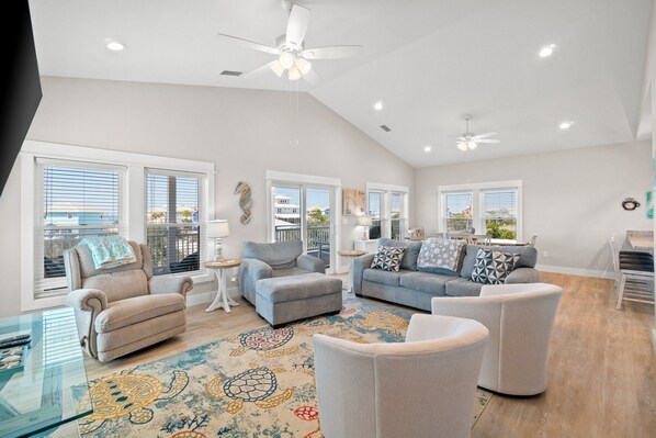 A spacious living room with a high ceiling, large windows, and a ceiling fan.
