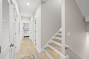 A modern hallway with wooden stairs, white walls, and a patterned rug.