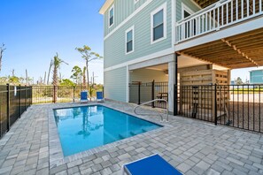 A swimming pool with a wooden deck and a covered area, surrounded by a fence.
